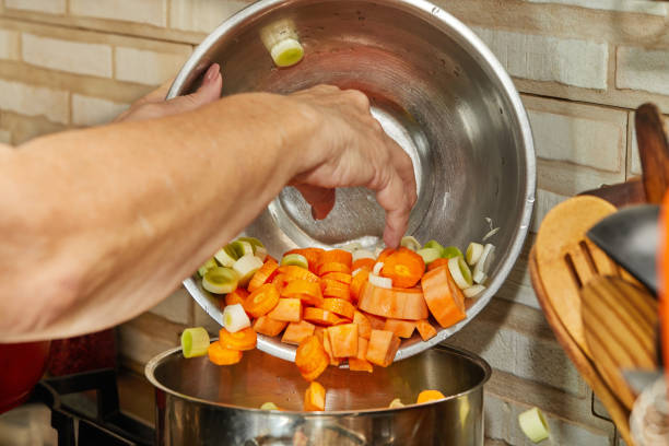 Chef pours onions, carrots and leeks from bowl into saucepan.