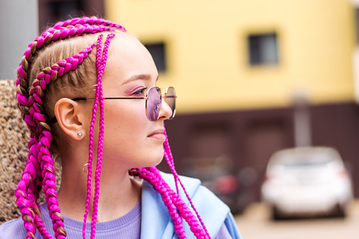 Portrait of a caucasian teenage girl with pink braids on a street background.Summer concept.Generation Z style.Selective focus,close-up,copy space.