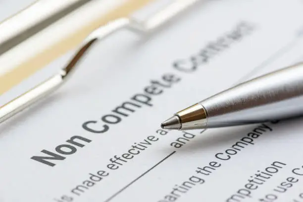 Photo of Blue ballpoint pen on a non compete contract. Noncompete contract is an agreement between employee and employer, not to enter into competition in subsequence business effort. Legal concept.