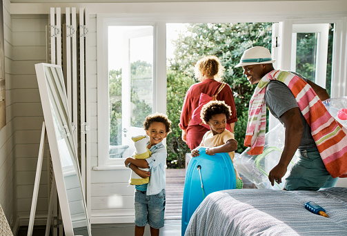 Father, mother and two sons excited to head out on a holiday or vacation getaway. Sibling brothers and their parents with towels and toys for an outing. Black family getting ready to go to the beach