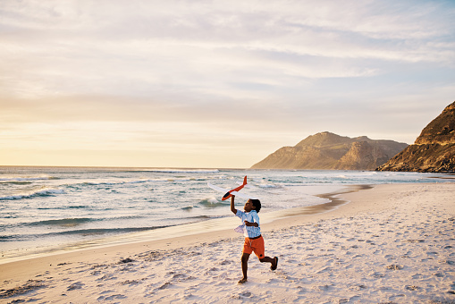 Little boy running with a toy on the beach with copy space. Child playing with an airplane plaything by the ocean on his holiday vacation. Playful, energized kid having fun with an outdoor activity