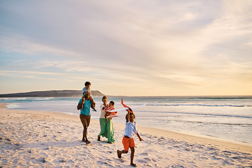 Young family walking on the beach together on the weekend. Loving parents on a walk with their children at the seashore during a vacation. Boy flying a plane and bonding with mom and dad on holiday