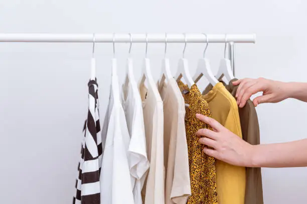 Woman choosing and picking out clothes to buy hanging on clothing rack in fashion store. Female clothes organized on clothes hangers. Shopping concept