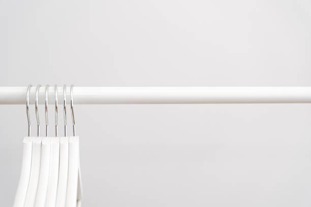 Empty white coat hangers on a clothing rack against white wall background stock photo