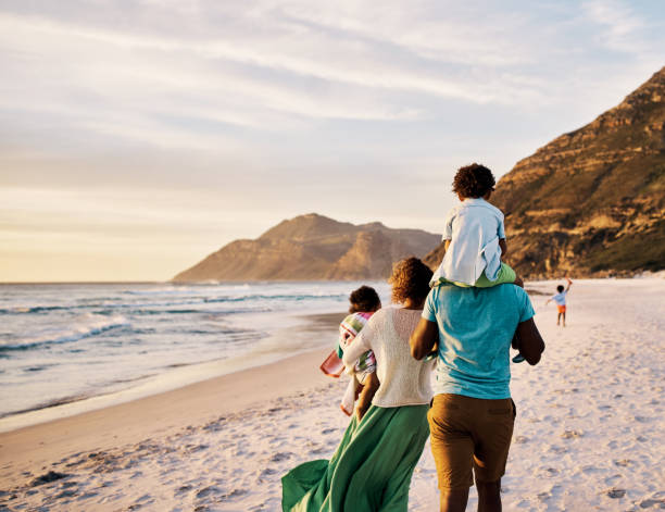 어린 아이들이 바다를 따라 묶고 산책하는 아프리카 부모. 여름 방학 또는 휴가 기간 동안 야외 활동을 즐기는 어린 아이들. 복사 공간이있는 해변을 걷는 가족의 뒷모습 - family vacation 뉴스 사진 이미지