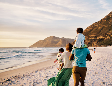 African parents with little kids bonding and strolling by ocean. Little children enjoying the outdoors during their summer holidays or vacation. Rear of a family walking on the beach with copy space