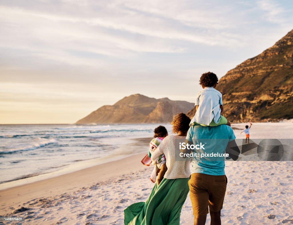 African parents with little kids bonding and strolling by ocean. Little children enjoying the outdoors during their summer holidays or vacation. Rear of a family walking on the beach with copy space Rear of a family walking on the beach with copy space. African parents with little kids bonding and strolling by ocean. Little children enjoying the outdoors during their summer holidays or vacation Vacations Stock Photo