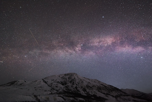 The galaxy hanging over snowcapped mountains at night.