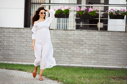 Walking woman. Beautiful model wearing fashionable summer white dress and white sunglasses