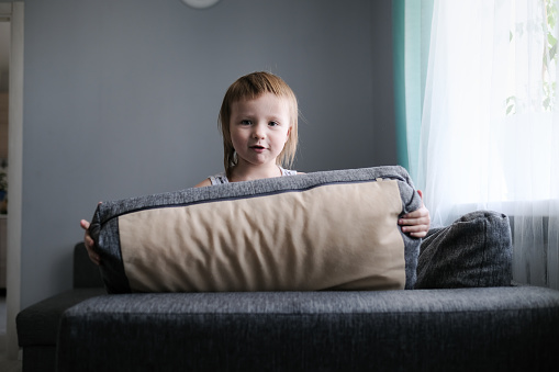 Kid Toddler builds house from pillows on sofa in living room, lifestyle and games in real interior