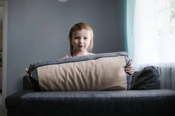 Photo of funny European child playing with pillows on couch