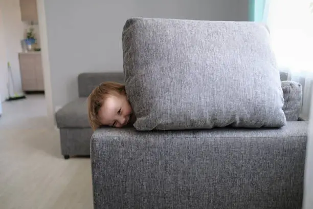 Photo of funny European child playing with pillows on couch