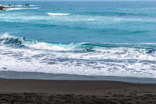 Waves with white foam on the crests of the sea with turquoise blue water and black sand on the beach. Coastline of Atlantic Ocean in the Canary Islands, Spain stock photo