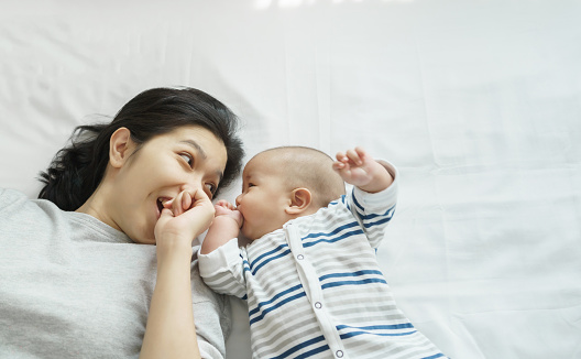 Loving Japanese Young mother playing with her little baby boy on bed at home, Happy mother's day.