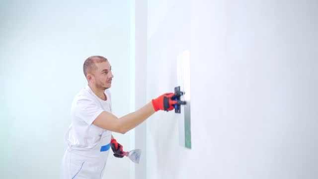 experienced repairman is plastering wall, using spatula, putty knife and white modern mortar, stuccoing. Portrait professional man putty plaster. skilled craftsman