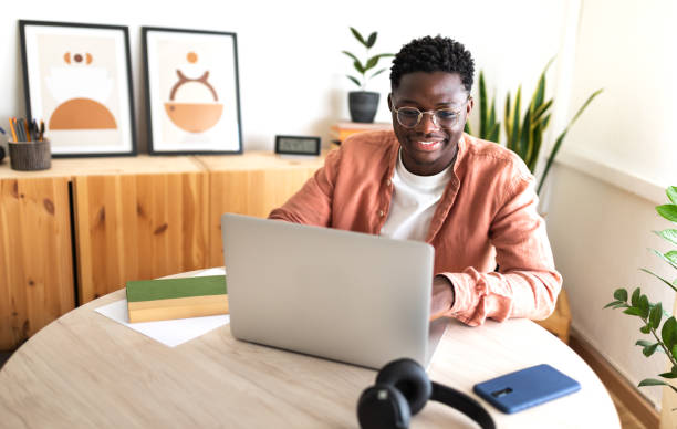ノートパソコンを使って自宅で勉強している幸せな黒人男子大生。 - learning male studying smiling ストックフォトと画像