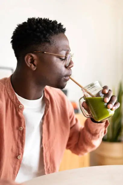 Photo of Vertical profile portrait of African American black man drinking healthy green juice with bamboo straw.