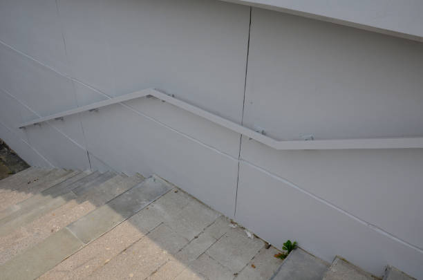 from the bottom of the handle is a recessed LED strip with yellow light. hidden built-in lamp shows a man's hand. the concrete side of the staircase with retaining walls runs through terrain of slope, beneath desde la parte inferior del mango hay una tira de led empotrada con luz amarilla. la lámpara incorporada oculta muestra la mano de un hombre. el lado de hormigón de la escalera con muros de contención corre a través de terreno de pendiente
