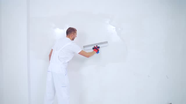 experienced repairman is plastering wall, using spatula, putty knife and white modern mortar, stuccoing. Portrait professional man putty plaster. skilled craftsman