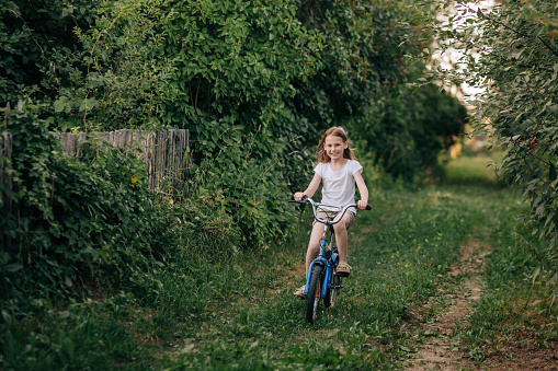 Smiling cute child girl riding a bicycle on the suburbs in summertime