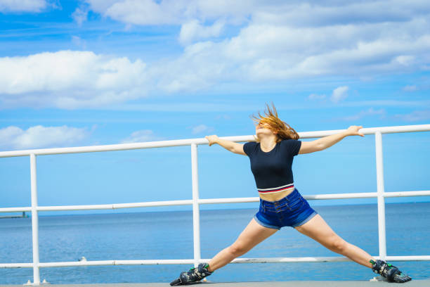 Attractive young woman wearing roller skates relaxing after ride. Fit female having fun during summer time on sea coast.