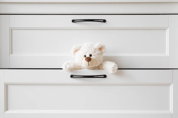Smiling white teddy bear looking from opened drawer at home. Closeup. Front view. stock photo