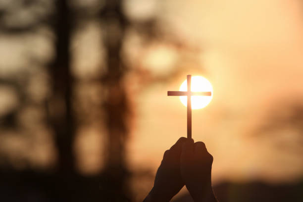 la luce del sole del cielo al tramonto e la sagoma di una croce in mano - cattolicesimo foto e immagini stock