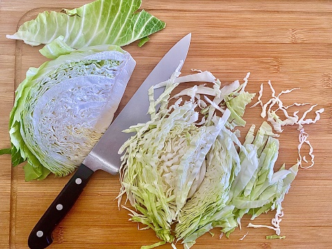 Horizontal flat lay of domestic kitchen counter with wood cutting board with ingredient of cut up green white cabbage as ingredient for coleslaw salad