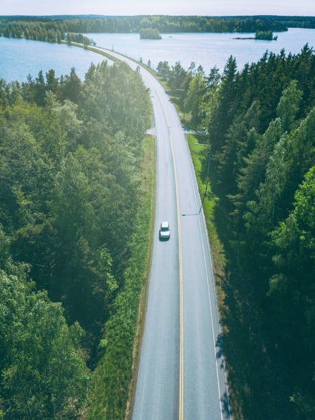 widok z lotu ptaka na wiejską drogę przez zielone lasy i niebieskie jeziora w finlandii - road winding road car country road zdjęcia i obrazy z banku zdjęć