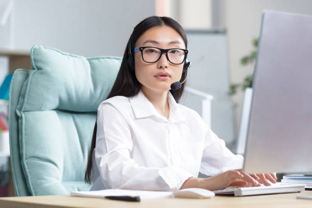 portrait of a young beautiful asian woman in headphones with a microphone - hotel reception customer service representative headset receptionist imagens e fotografias de stock