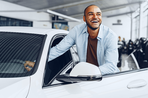 Portrait of a handsome happy African American man sitting in his newly bought car close up
