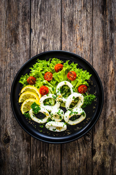 Fried calamari rings with lemon, greens and cherry tomatoes on wooden table Fried calamari rings with lemon, greens and cherry tomatoes on wooden table seafood salad stock pictures, royalty-free photos & images