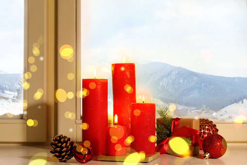 Red burning candles, gift box and festive decor on window sill indoors. Christmas eve