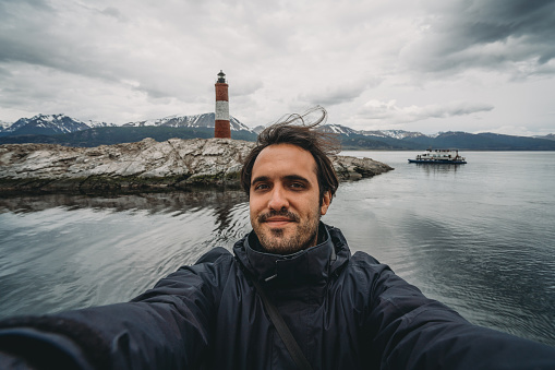 Man taking a selfie close to Les Eclaireurs Lighthouse near Ushuaia. The lighthouse is 5 nautical mile east of Ushuaia in the Beagle Channel, Tierra del Fuego, southern Argentina.