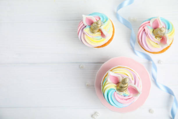 istock Cute sweet unicorn cupcakes on white wooden table, flat lay. Space for text 1408195783
