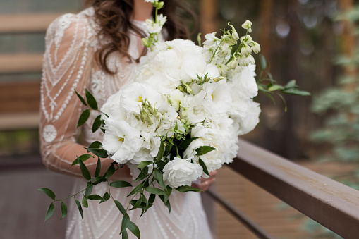 Bride with white wedding bouquet. Woman in white dress holding bouquet with peonies, lisianthus eustoma and ruscus. Happy wedding concept