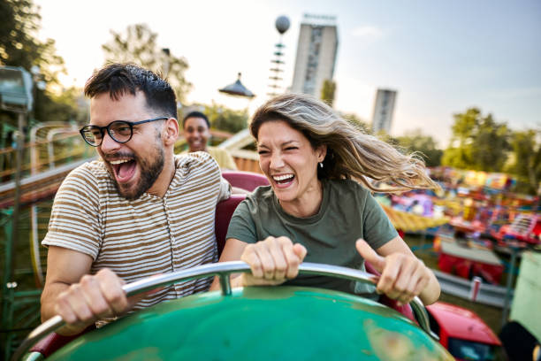 Young cheerful couple having fun on rollercoaster at amusement park. Cheerful couple having fun while riding on rollercoaster at amusement park. amusement park stock pictures, royalty-free photos & images