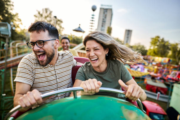 young cheerful couple having fun on rollercoaster at amusement park. - lunapark treni stok fotoğraflar ve resimler