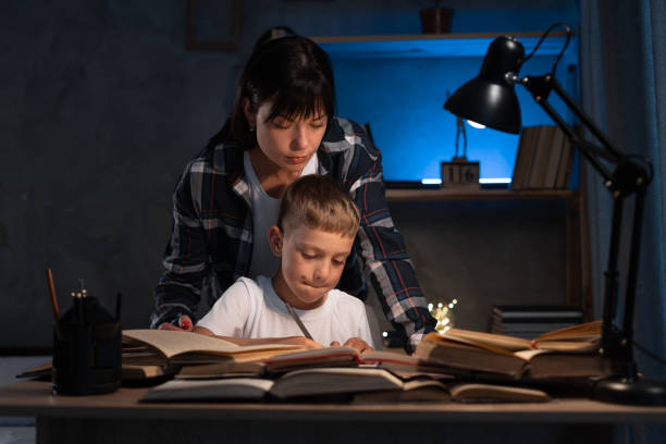 istock Cute boy with mother doing homework at home at night using books. online schooling 1408200332