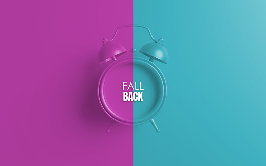 Alarm clock with Fall Back written sign against purple and blue background. Easy to crop horizontal composition for all your social media and print sizes with copy space.