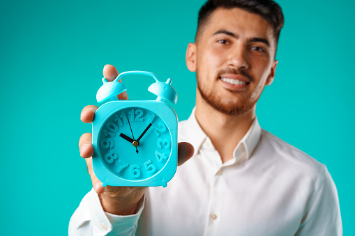 Young mixed race businessman showing alarm clock against blue background