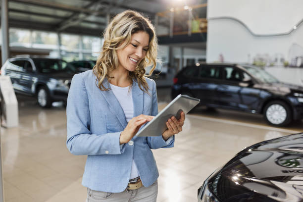 happy car salesperson using digital tablet in a showroom. - verkoopster stockfoto's en -beelden