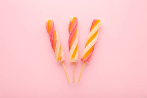 Three colorful fruit ice popsicles on sticks. Light pink table background. Pastel color. Closeup. Cold sweet snack in summer. Top down view.