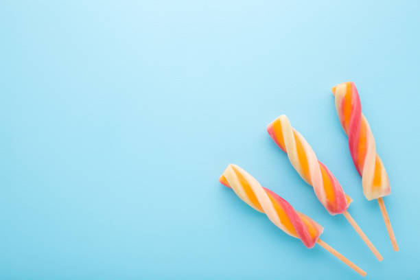 Three colorful fruit ice popsicles on sticks. Light blue table background. Pastel color. Closeup. Cold sweet snack in summer. Empty place for text. Top down view.