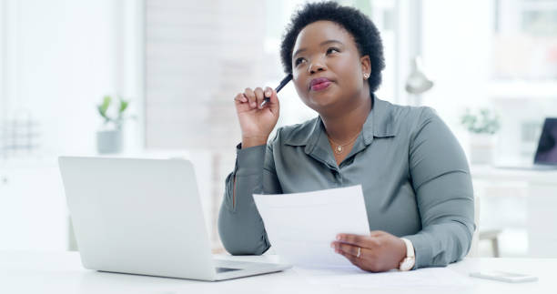 istock One young businesswoman thinking of ideas while reading paperwork report and browsing internet on laptop in an office. Entrepreneur brainstorming decisions while planning for success in startup agency 1408202853