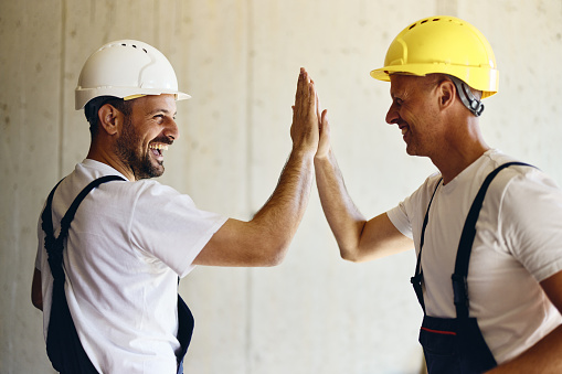 Cheerful construction workers giving each other high-five during home renovation process.