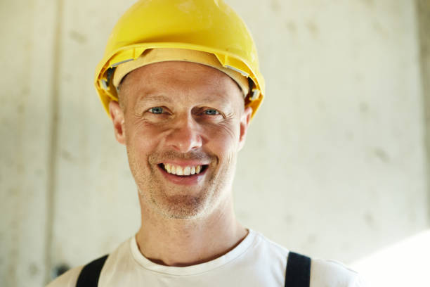 cheerful engineer wearing a reflective orange safety vest and hard hat celebrates by clenching his fists towards the camera at a construction site. The image captures a moment of joy and triumph