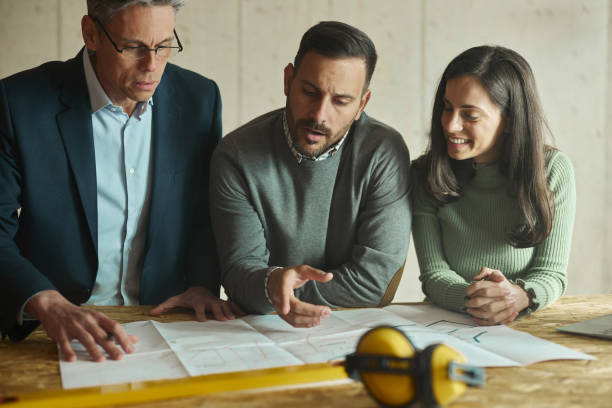 istock Young couple and their agent examining blueprints at construction site. 1408203610