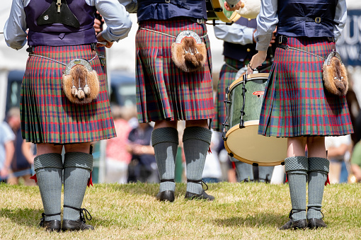 3rd July 2022: Scottish Game Fair. Rear view of a Highland Pipe Band playing at a traditional Scottish Game Fair in Perth. The pipe band have bagpipers and drummers. They are wearing traditional Highland dress, with kilts, sporrans and a traditional Scottish knife called a Sgian Dubh, tucked in their green wool socks.