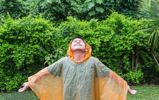 Asian boy wearing orange raincoat is happy and having fun in the rain on a rainy day.